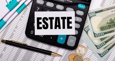 On the desktop are reports, a pen, cash, a calculator and a card with the text ESTATE. Business concept