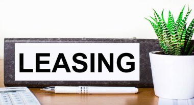 On a wooden table there is a folder for documents with a LEASING dough, a green plant in a pot, a pen and a calculator. Business concept.