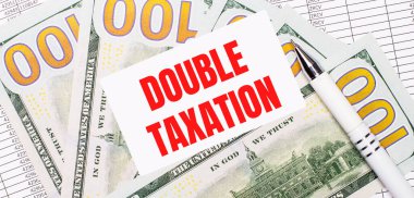 Against the background of reports and dollars - a white pen and a card with the text DOUBLE TAXATION. Business concept