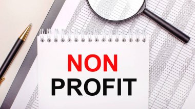 Desktop magnifier, reports, pen and notebook with text NON PROFIT. Business concept