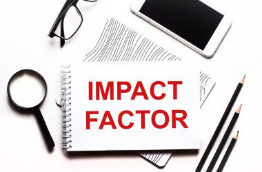 Beyaz bir arka plan gözlüğü, bir büyüteç, kalemler, bir akıllı telefon ve IMPACT FACTOR yazılı bir defter.