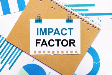 Masaüstünde mavi ve açık mavi grafikler ve diyagramlar, kahverengi bir defter ve mavi ataçlı bir kağıt ve IMPACT FACTOR metni bulunmaktadır. Yukarıdan bak. İş konsepti
