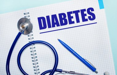 Açık mavi arka planda DiABETES, mavi kalem ve steteskop yazılı açık bir defter var. Yukarıdan bak. Tıbbi konsept