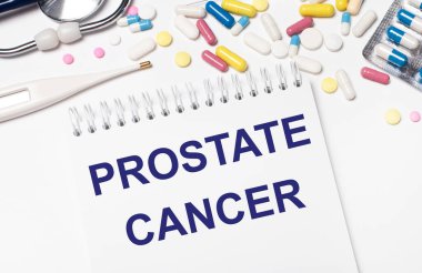 Açık bir arka planda, çok renkli haplar, bir steteskop, bir elektronik termometre ve içinde PROSTATE CANCER yazan bir defter. Tıbbi konsept.