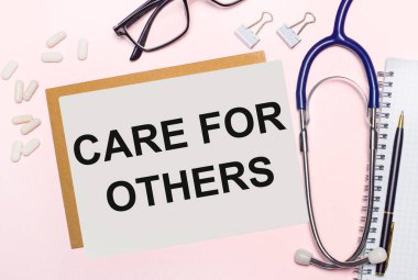 Açık pembe bir arkaplanda, steteskop, beyaz haplar ve kağıt raptiyeler, siyah çerçeveli gözlükler ve diğerleri için yazı özeti olan bir kağıt. Yukarıdan bak. Tıbbi konsept