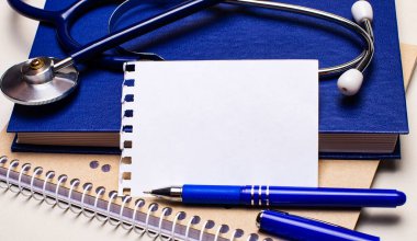 Masanın üzerinde not defterleri, bir steteskop, bir kalem ve metin eklemek için boşluğu olan bir kağıt var. Tıbbi konsept