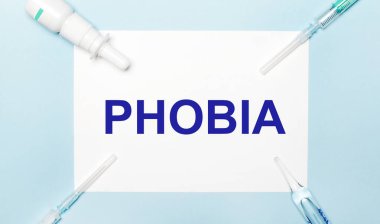 Açık mavi arka planda, şırıngalar, ilaç şişesi, ampul ve PHOBIA yazılı beyaz bir kağıt. Tıbbi konsept.