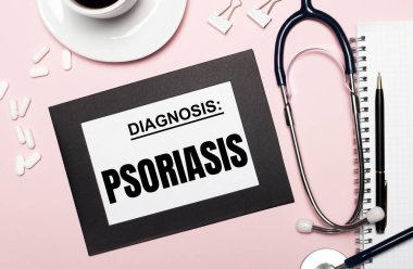 Açık pembe arka planda, kalem, steteskop, beyaz haplar, ataç ve PSORIASIS yazılı bir kağıt olan bir defter. Tıbbi konsept