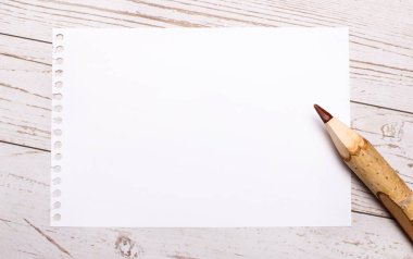 On a light wooden background, a colored pencil and a white blank sheet of paper with a place to insert text. Template