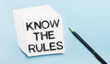 On a light blue background, there is a black pen and a stack of white note paper with the text KNOW THE RULES