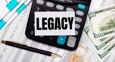 On the desktop are reports, a pen, cash, a calculator and a card with the text LEGACY. Business concept