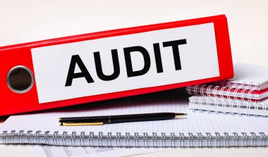 Masaüstünde defterler, bir kalem ve AUDIT yazılı kağıtlar için kırmızı bir klasör var. İş konsepti