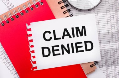 Hafif bir arkaplanda - raporlar, bir büyüteç, kahverengi ve kırmızı not defterleri ve CLAIM DENIED yazılı beyaz bir not defteri. İş konsepti