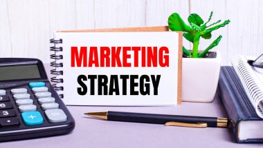 Masaüstünde bir hesap makinesi, günlükler, saksı bitkisi, bir kalem ve üzerinde MARKETING STRATEGY yazan bir defter var. İş konsepti. İş yeri kapanıyor.