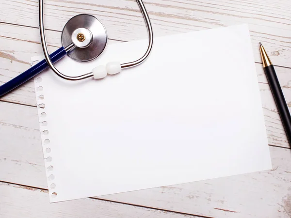 在一张轻薄的木制桌子上 有一个听诊器 一支钢笔和一张纸 上面有一个地方可以插入文字 医疗概念 — 图库照片