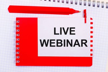Beyaz bir not defterinde, kırmızı bir kalem, kırmızı bir not defteri ve üzerinde LIVE WEBINAR yazan beyaz bir sayfa.