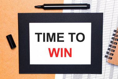 Ahşap bir masada, siyah açık bir kalem, kahverengi bir not defteri ve siyah çerçeveli Time to WIN yazılı bir kağıt var. Yukarıdan görüntüle.