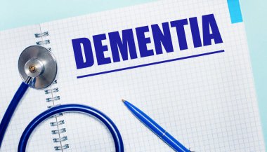 Açık mavi arkaplanda DEMENTIA, mavi kalem ve stetoskop yazılı açık bir defter var. Yukarıdan bak. Tıbbi konsept