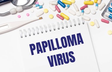Açık bir arka planda, çok renkli haplar, steteskop, elektronik termometre ve PAPILLOMA VIRUS yazılı bir defter. Tıbbi konsept.