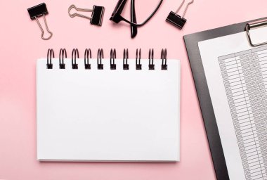 Pembe bir arkaplanda, raporlar, siyah ataçlar, gözlükler ve metin eklemek için yeri olan boş bir defter.