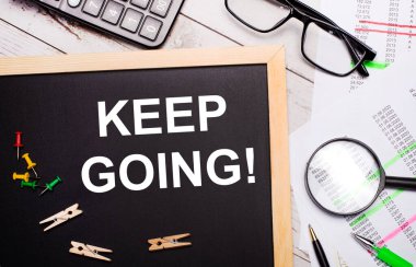 Masaüstünde bir hesap makinesi, raporlar, gözlükler, bir büyüteç, kalemler ve mandallı bir pano ve KEEP İş Yapma Konsepti var.