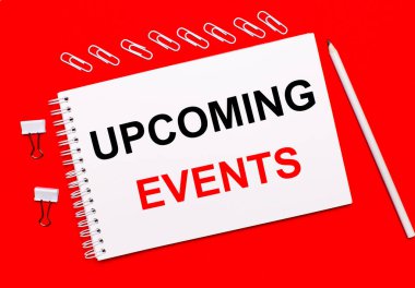 Parlak kırmızı bir zemin üzerinde, beyaz bir kalem, beyaz ataçlar, ve beyaz bir defter UPCOMING etkinlikleri yazılı.