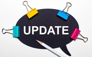 Açık arkaplanda, çok renkli ataçlar, üzerinde UPDATE yazan beyaz bir kalem ve siyah kağıt. Yukarıdan görüntüle