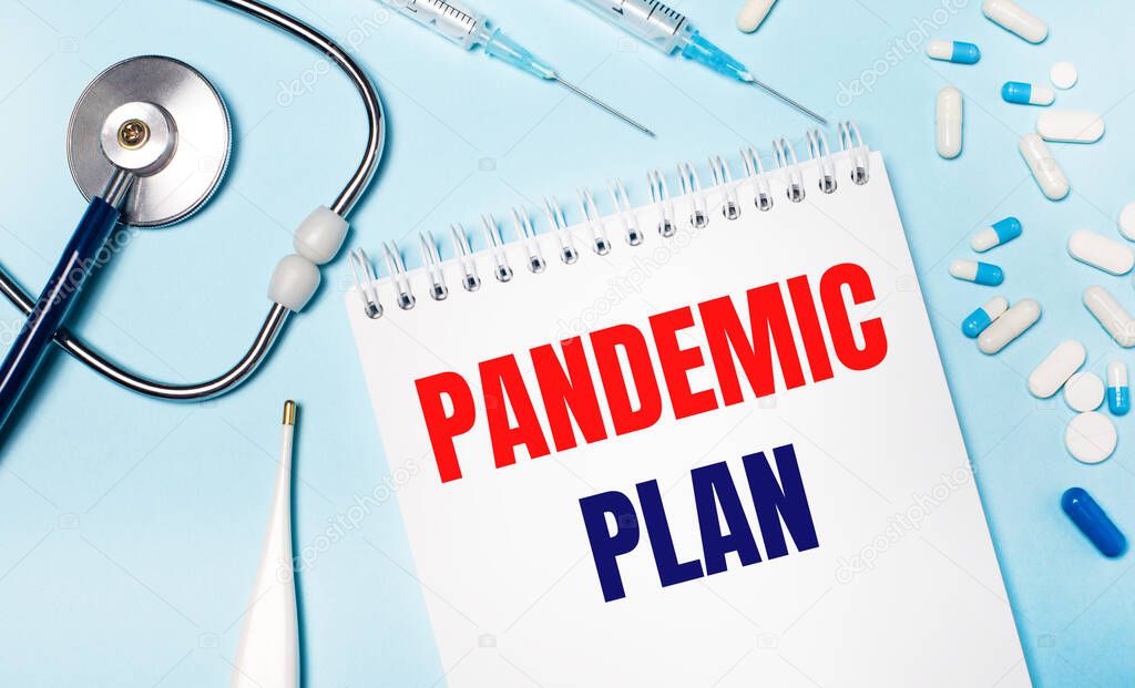 On a light blue background, an electronic thermometer, a stethoscope, white and blue pills, syringes and a notebook with the text PANDEMIC PLAN. Medical concept