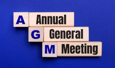 Parlak mavi arkaplanda, beyaz tahta bloklar ve AGM Yıllık Genel Toplantısı metni içeren küpler.