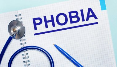 Açık mavi arka planda, üzerinde PHOBIA, mavi kalem ve stetoskop olan açık bir defter. Yukarıdan bak. Tıbbi konsept