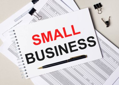 Masaüstünde belgeler, kalem, siyah ataçlar ve içinde SMALL BUSINESS metni olan bir defter var. İş konsepti
