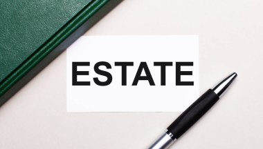 Açık gri arka planda bir kalem, yeşil bir defter ve üzerinde 