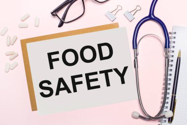 Açık pembe bir arkaplanda, steteskop, beyaz haplar ve ataçlar kağıt için, siyah çerçeveli gözlük ve metin FOOD Safty ile bir sayfa kağıt. Yukarıdan bak. Tıbbi konsept