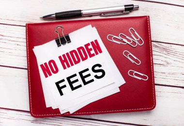 Hafif ahşap bir arka planda, bordo bir kalem ve defter. Defterde beyaz ataçlar ve gizli ücretler olmayan beyaz kağıtlar var. İş konsepti