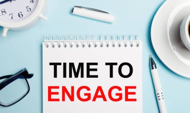 Açık mavi arka planda, kahveli beyaz bir kupa, beyaz bir çalar saat, beyaz bir kalem ve 