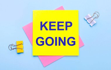 Açık mavi arkaplanda sarı ve beyaz ataçlar, pembe ve sarı yapışkan notlar var.