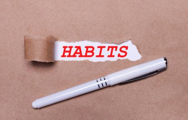 Kraft kağıdında, beyaz bir kalem ve beyaz bir kağıt şeridi HABITS yazılı..