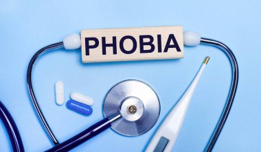 Açık gri arka planda, stetoskop, elektronik termometre, haplar, PHOBIA yazılı tahta blok. Tıbbi konsept.