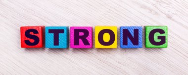 Açık ahşap arka planda, üzerinde STRONG yazılı çok renkli tahta küpler var..