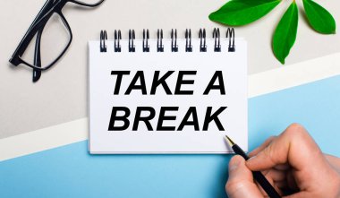 Gri-mavi arka planda, gözlüklerin yanında ve bir bitkinin yeşil yaprağında bir adam bir kağıt parçasına 