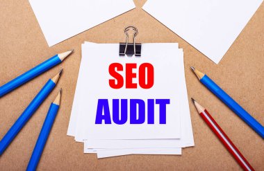 Açık kahverengi arka plan, mavi ve kırmızı kalemler ve SEO AUDIT yazılı beyaz kağıt üzerinde