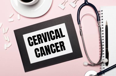 Açık pembe arka planda, kalem, steteskop, beyaz haplar, ataçlar ve CERVICAL CANCER yazılı bir kağıt olan bir defter. Tıbbi konsept