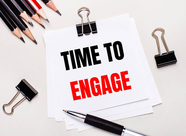 На светлом фоне черные карандаши, черные скрепки, ручка и лист белой бумаги с текстом TIME TO ENGAGE.