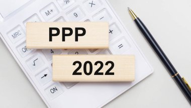 Tahta bloklar ve PPP 2022 beyaz bir hesap makinesinin arka planında yatar. Yakınlarda siyah bir kol var. İş konsepti