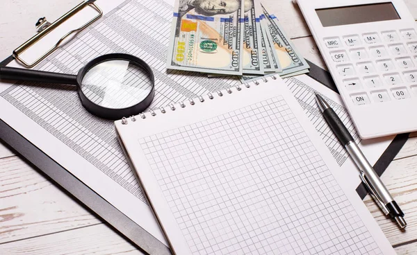 On the office table there are reports, black-rimmed glasses, dollars, a calculator, a magnifying glass, and a notebook with a pen. Business concept. Workplace close up