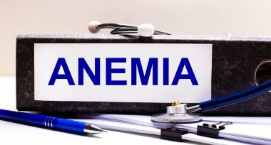 Masaüstünde stetoskop, mavi bir kalem ve ANEMIA metninin olduğu gri bir dosya klasörü var. Tıbbi konsept