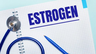 Açık mavi arka planda, üzerinde ESTROGEN yazan açık bir defter, mavi bir kalem ve stetoskop. Yukarıdan bak. Tıbbi konsept