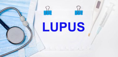Hafif arka planda bir stetoskop, bir elektronik termometre, bir şırınga, bir yüz maskesi ve LUPUS yazılı bir kağıt vardır. Tıbbi konsept