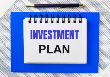 Masaüstündeki raporların arka planında mavi bir not defteri var. Üzerinde INVESTMENT planının olduğu bir kalem ve beyaz bir defter var. İş konsepti