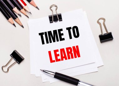 Açık pembe arka planda, açık mavi kalemler, ataçlar ve üzerinde 